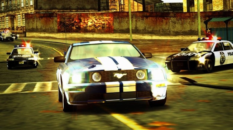 Egy kék Ford Mustangot üldöznek rendőrautók egy városon keresztül a Need for Speed: Most Wanted játékban