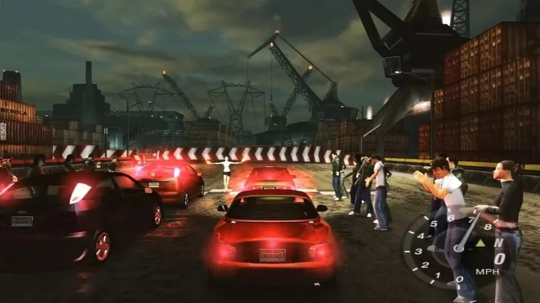 Sportautók csoportja sorakozik fel a kikötőknél, miközben a tömeg tapsol a Need for Speed: Underground 2-ben