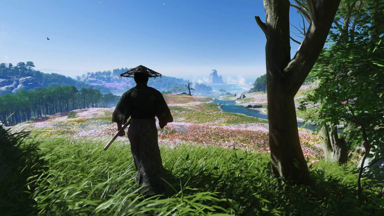 Egy szamuráj virágok és hegyek színes kilátására néz a Ghost of Tsushima városában