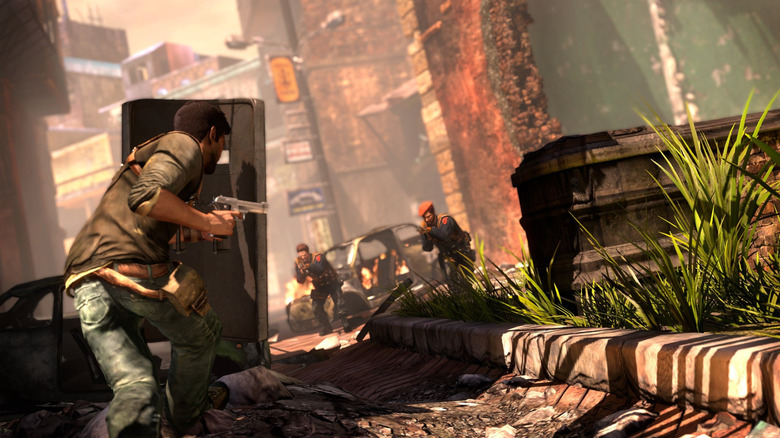 Nathan Drake fedezékbe bújik az előrenyomuló fegyveresek elől az Uncharted 2: among Thieves egyik utcájában