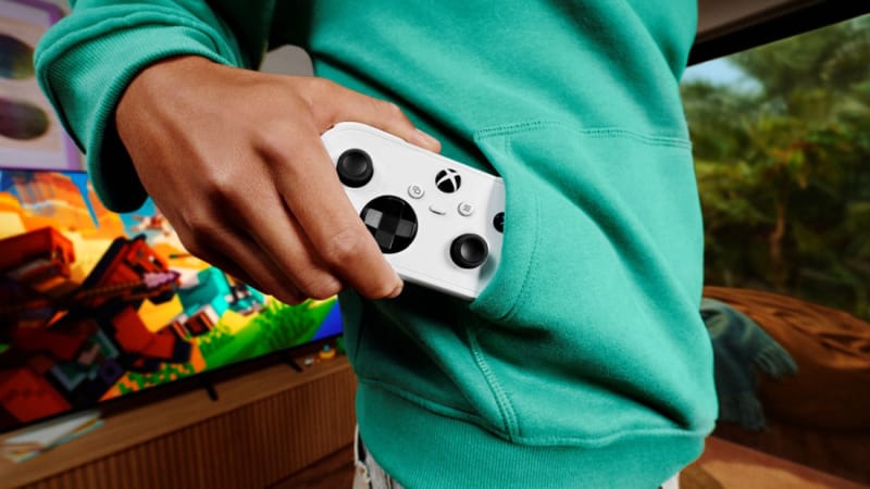 Az Xbox Nano Controller 2-es zsebméretűre csökkenti a játékot Az Xbox Nano kontrollert egy kézben tartva egy okostelefon mellett, hogy megmutassa a zsebméretű lábnyomát