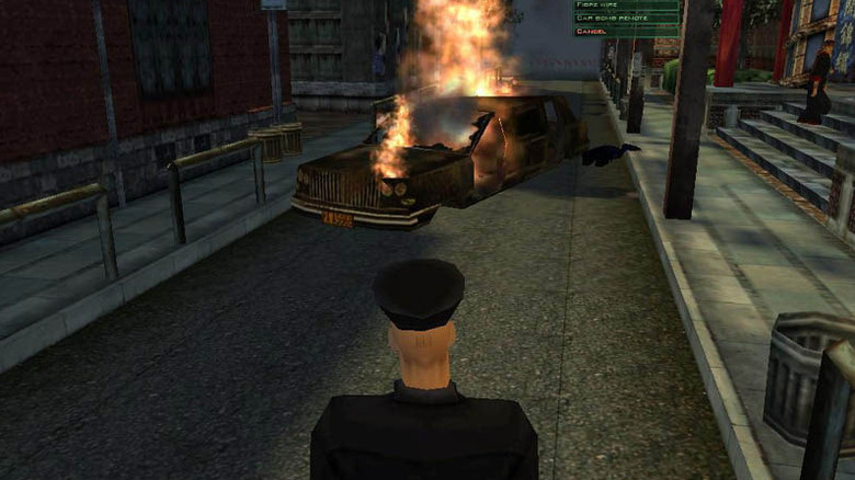 A sofőr egyenruhát viselő 47-es ügynök egy égő autót néz a Hitman: Codename 47-ben